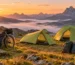 Dos tiendas de campaña ultraligeras verde lima, una de tipo túnel y otra de tipo iglú, montadas en un prado de montaña al amanecer junto a una bicicleta gravel con bolsas de bikepacking y dos mochilas de trekking